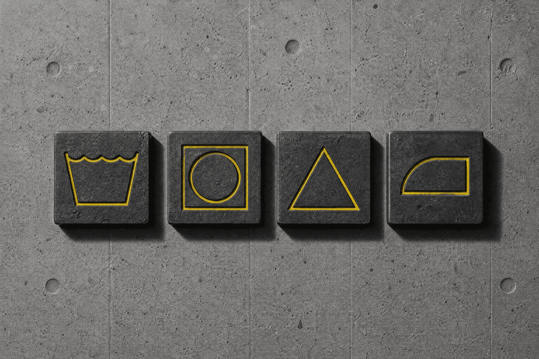 A row of small steel tiles laid on concrete, each embossed with a simple care symbol picked out in yellow