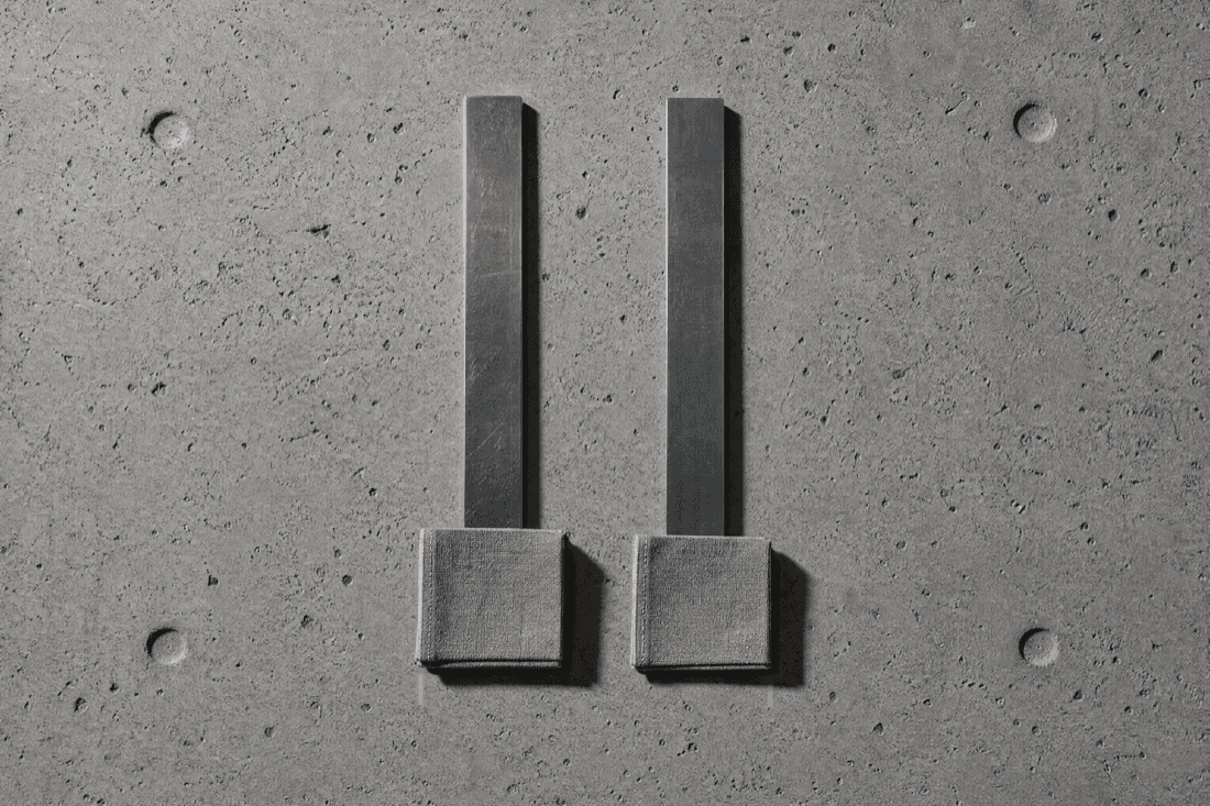 Two rules laid side by side on concrete with a fabric swatch squared against each, the right one falling slightly short
